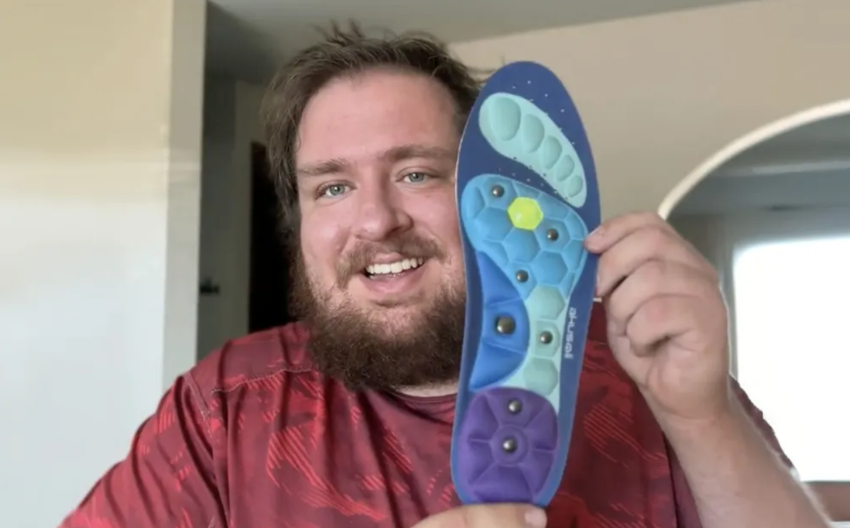 A smiling man holds up an insole in a home environment.