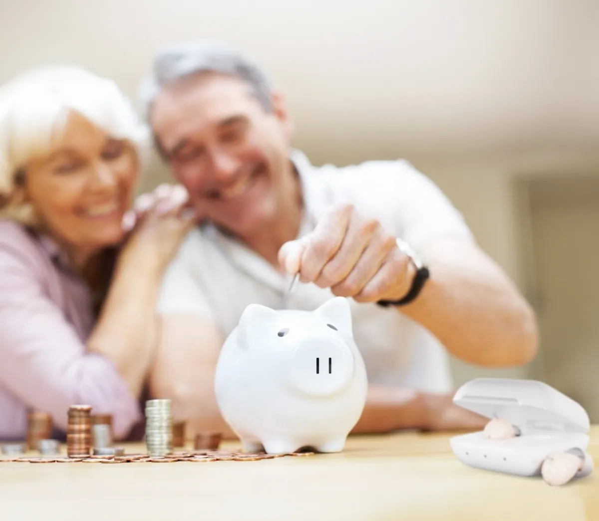Older couple smiling with piggy bank and hearing aid case visible