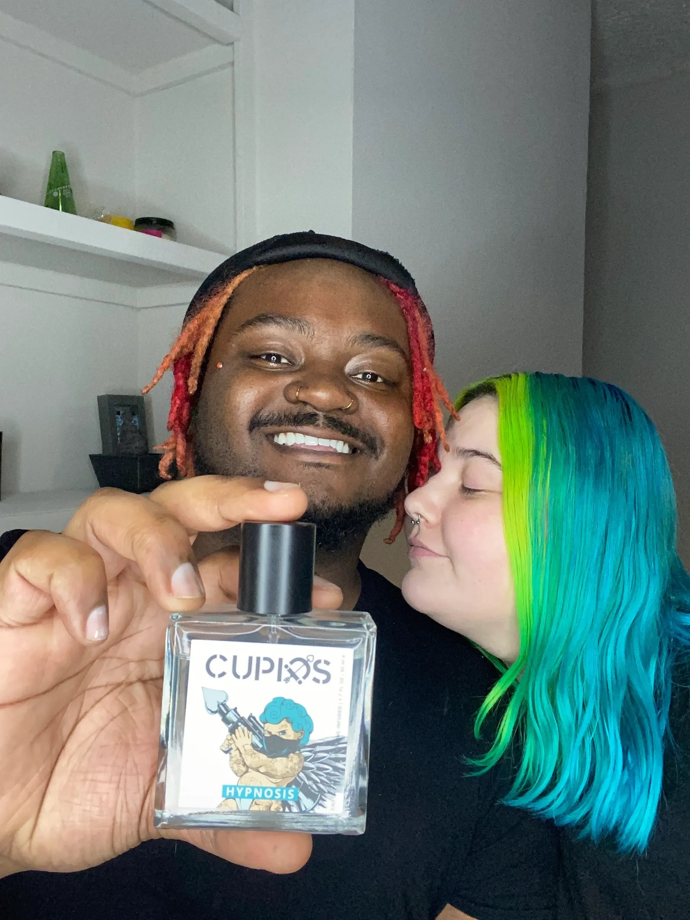 A person holding a bottle of Cupids Hypnosis perfume with a couple in the background