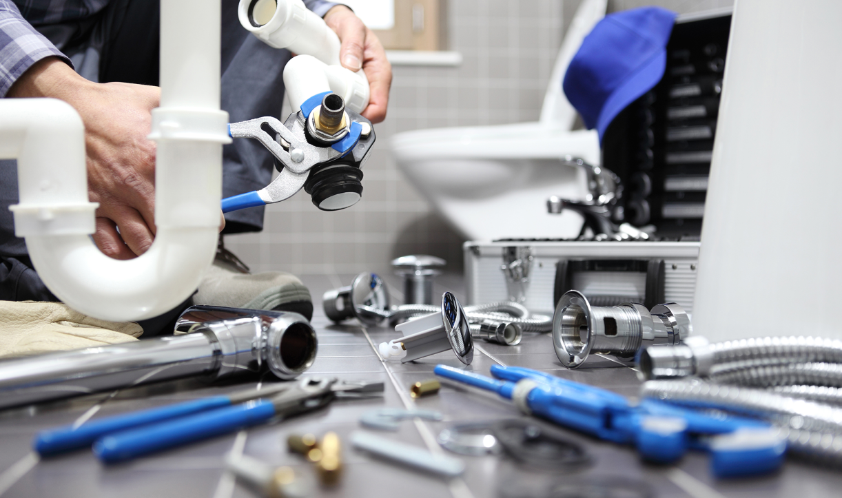 Person using a wrench to work on plumbing parts on a bathroom floor