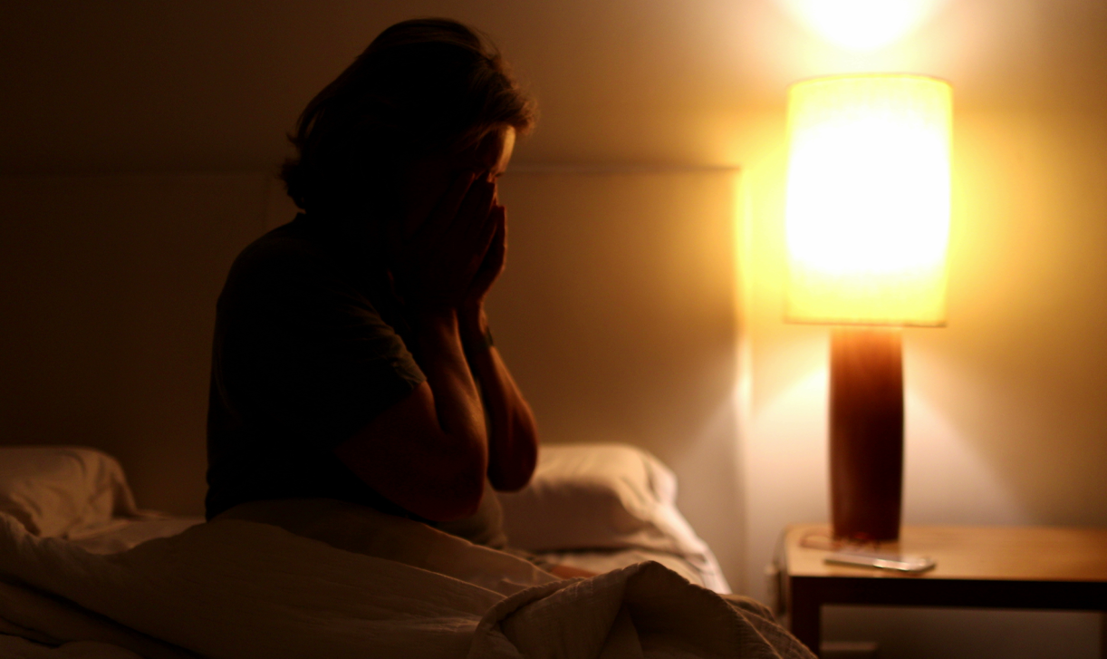 Customer photo of a person sitting on a bed in a dimly lit room