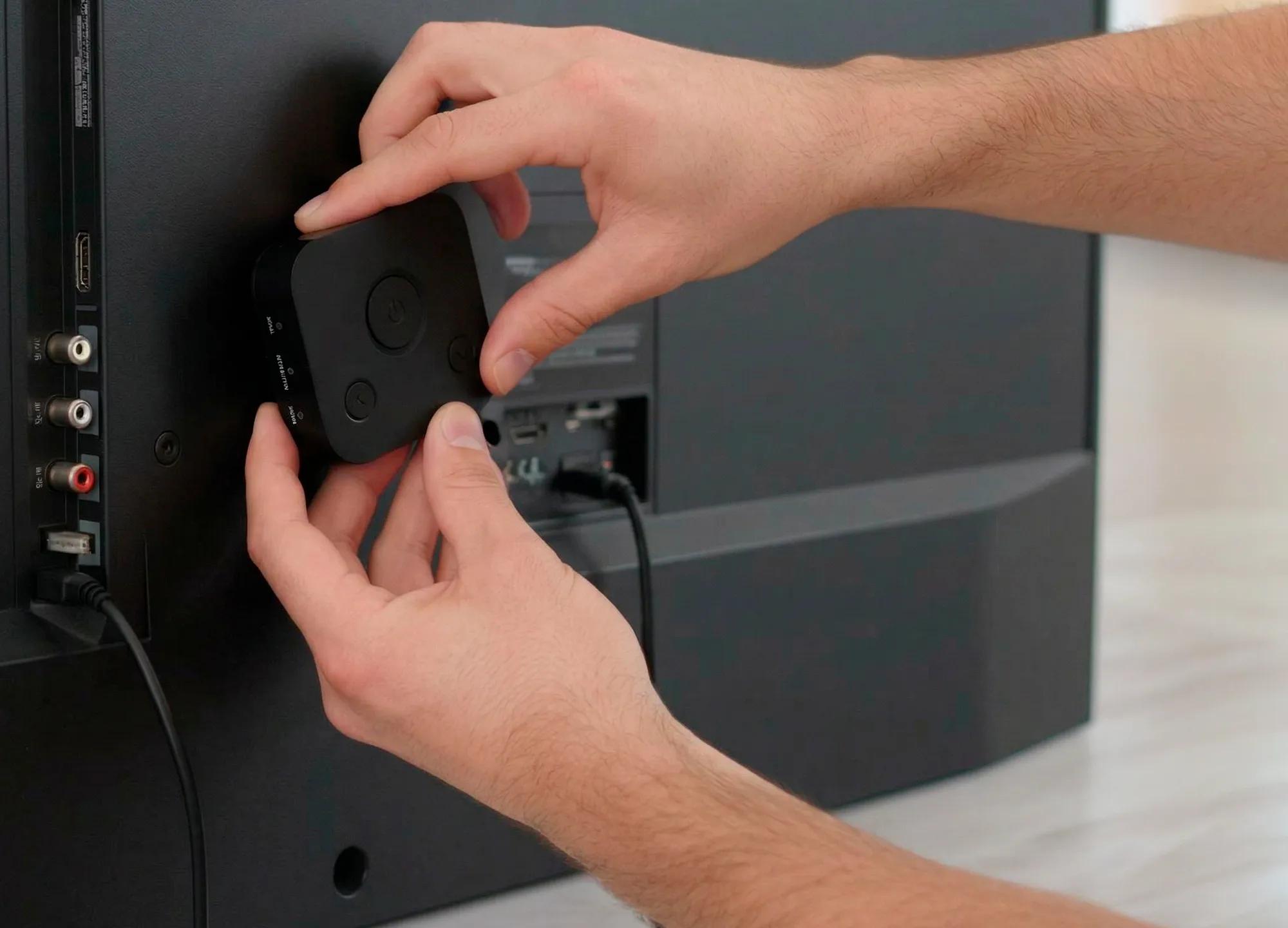 Hands plugging HearDirect transmitter into the back of a TV