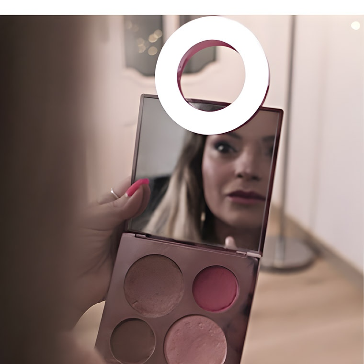 Person using a ring light attached to a makeup mirror while applying makeup