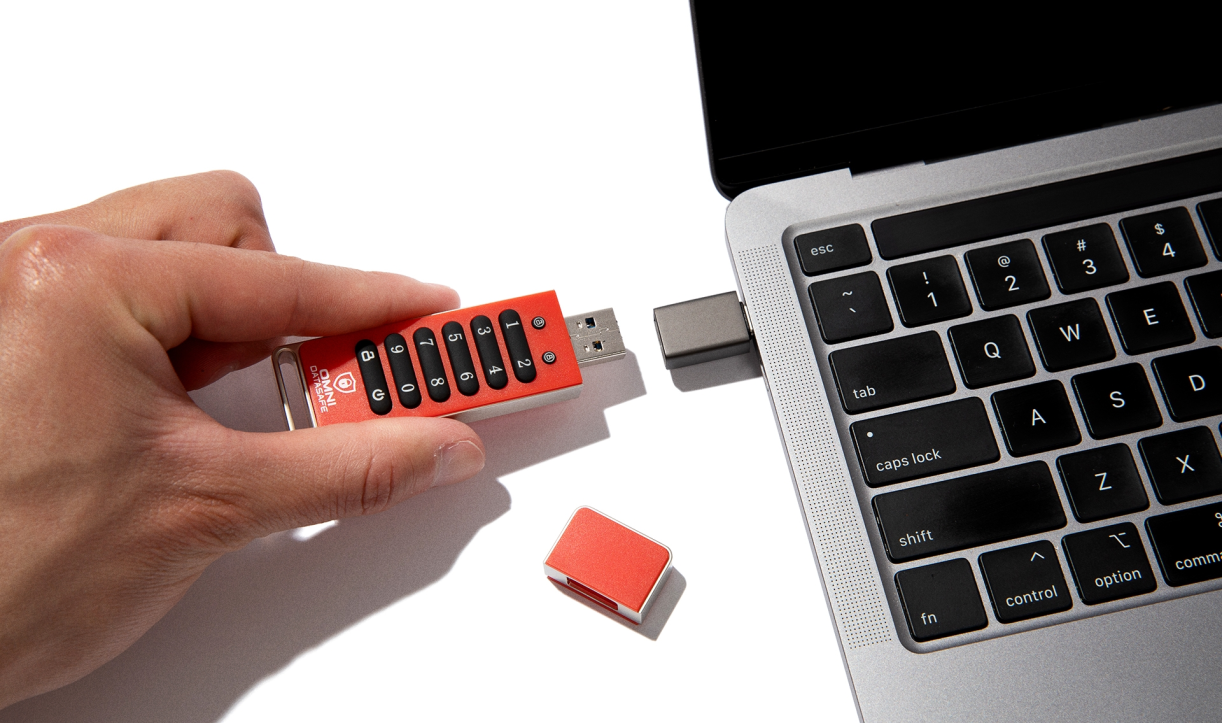 Hand plugging a keypad-secured Omni DataSafe USB drive into a laptop