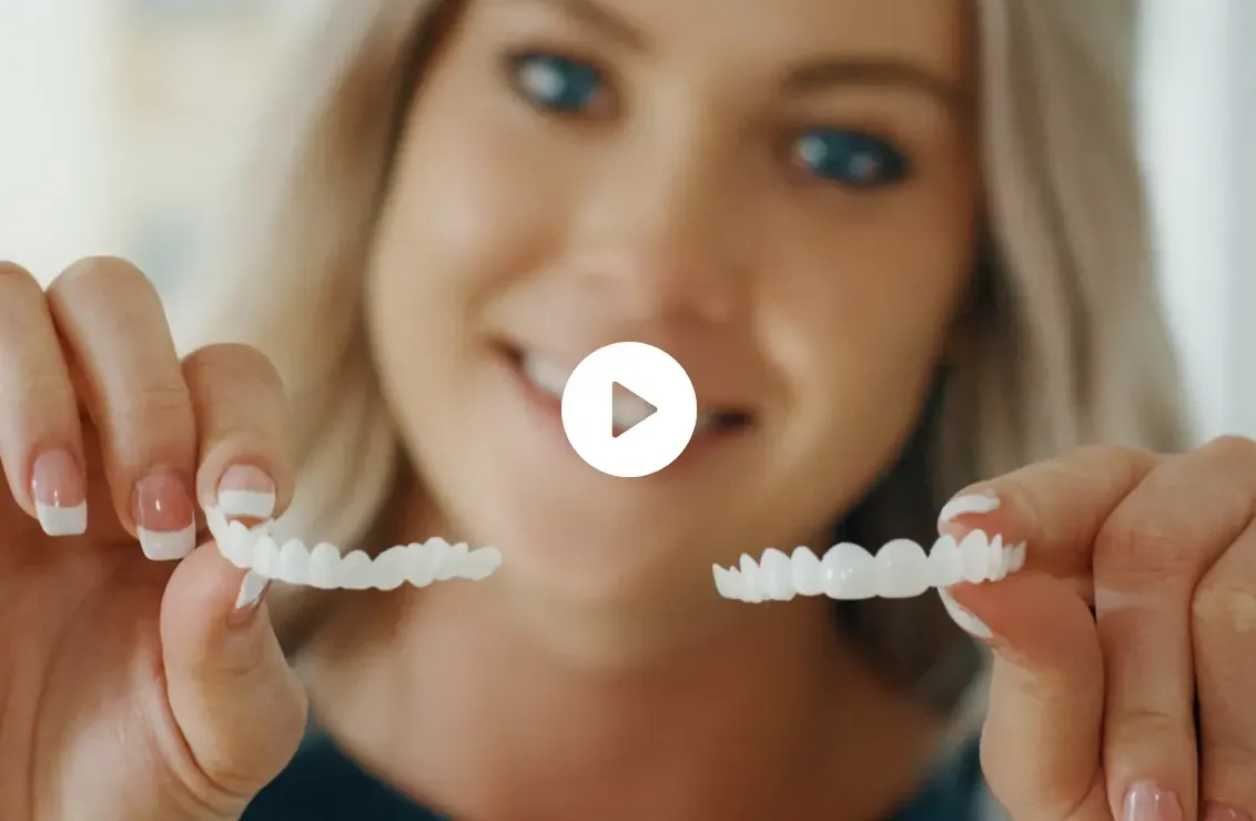 A woman holding up two dental veneers and smiling