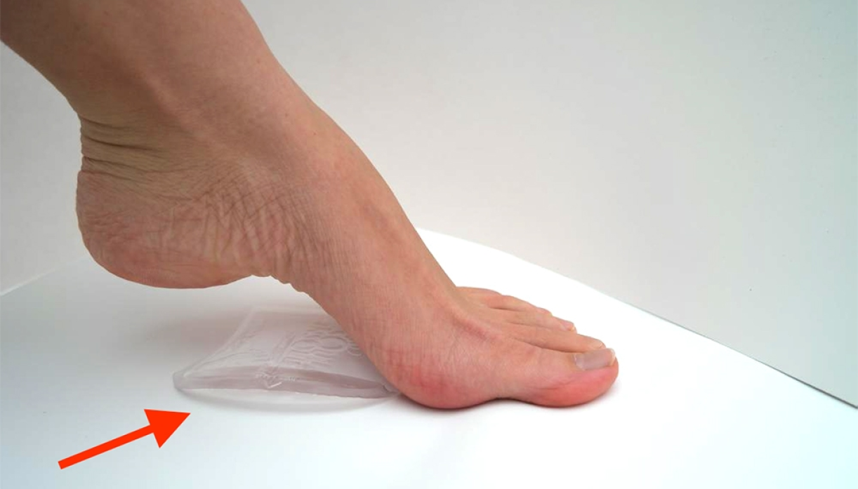 A person pressing their bare foot onto a gel insole with a red arrow pointing to the insole