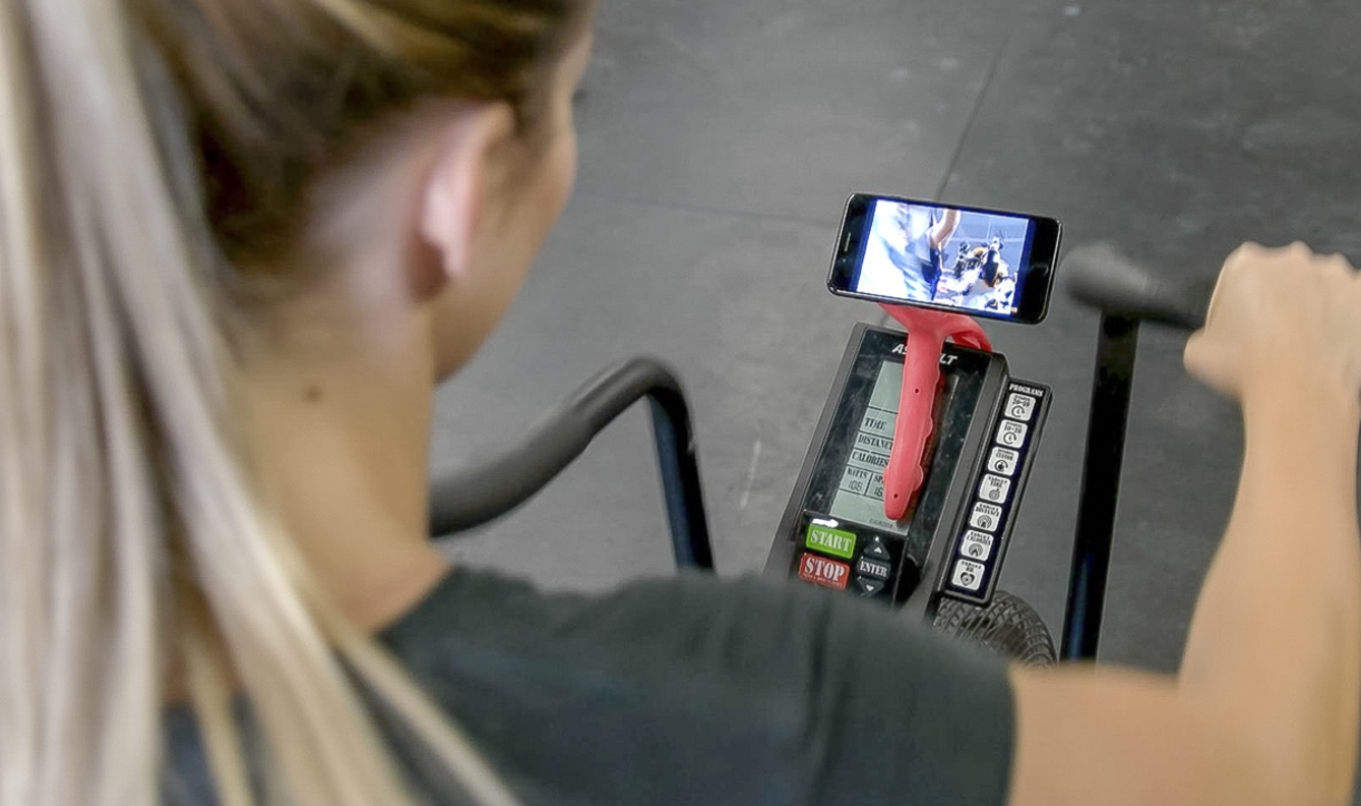 Tenikle holding a phone on exercise equipment during a workout