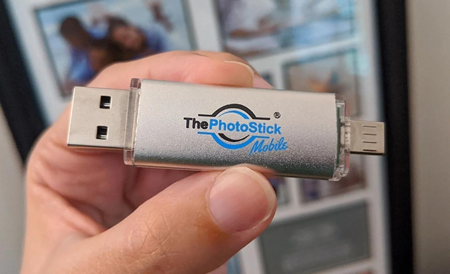 Close-up of a hand holding ThePhotoStick Mobile device in front of blurred photos