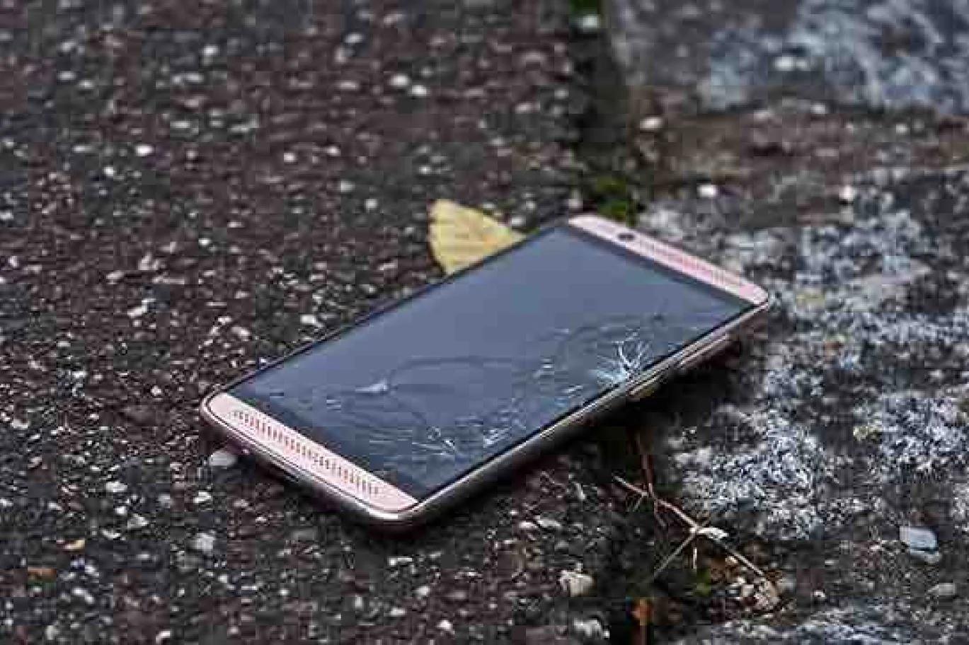 Smartphone with a cracked screen lying on pavement outdoors