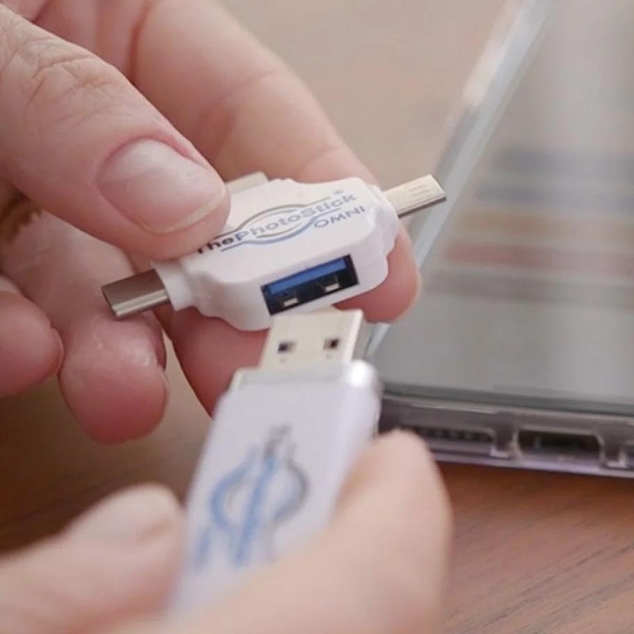 Close-up of hands holding ThePhotoStick OMNI device near a laptop