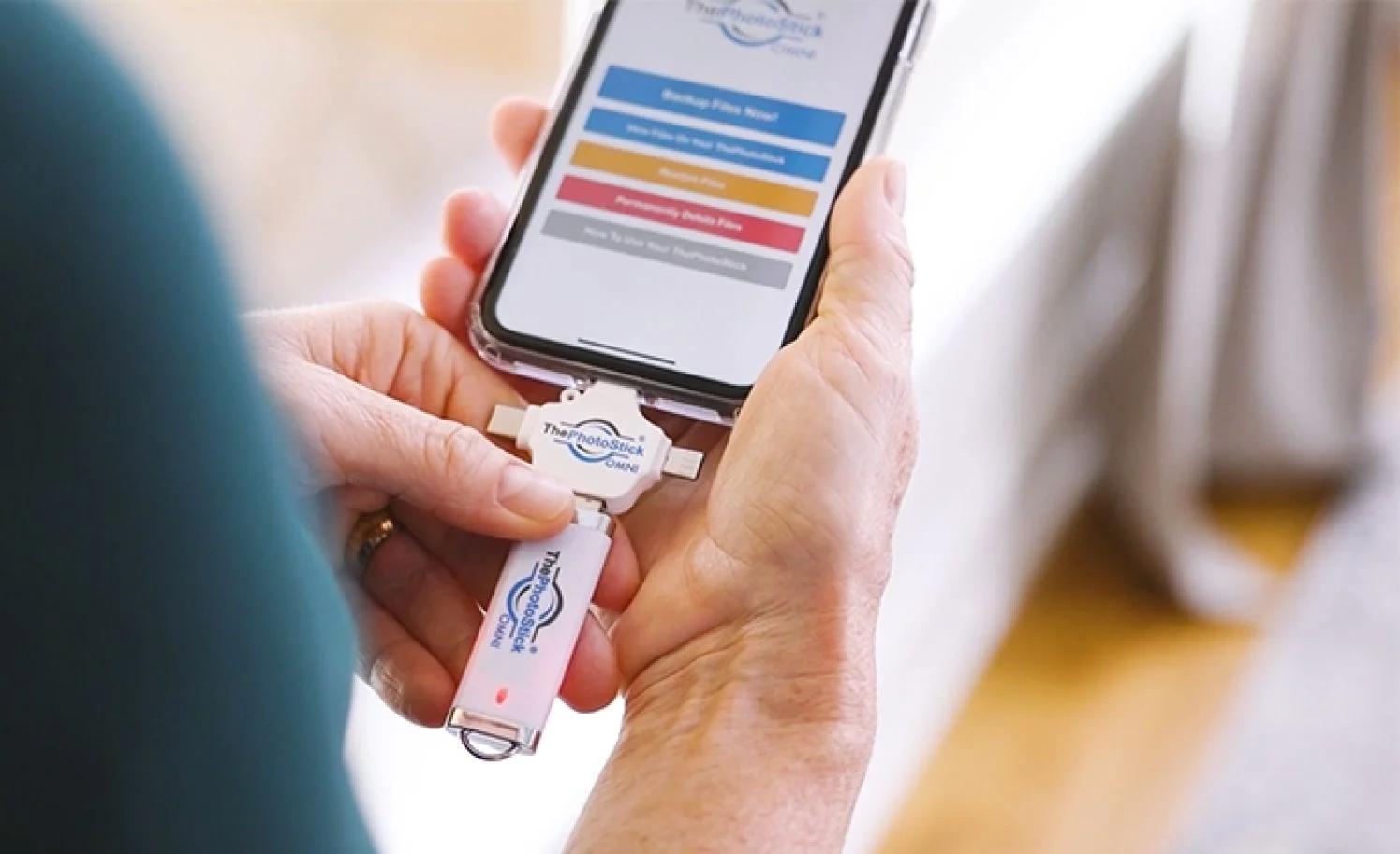 Person using ThePhotoStick OMNI with a smartphone displaying the backup app