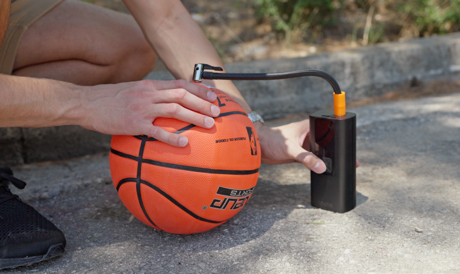 Person using TireHero's needle adapter to inflate a basketball outdoors