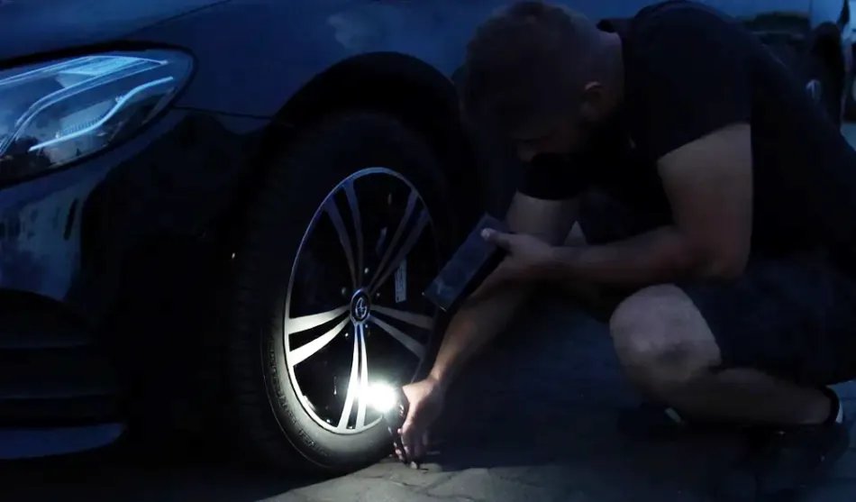 Person using the TireHero's flashlight to illuminate a car wheel at night