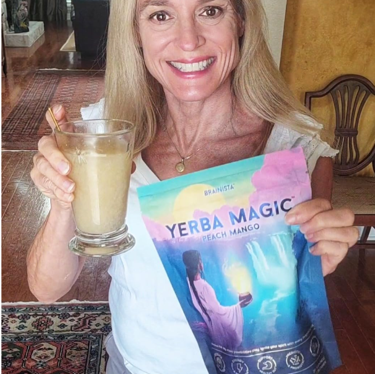 A smiling woman holding a glass of prepared drink and a bag of Yerba Magic Peach Mango